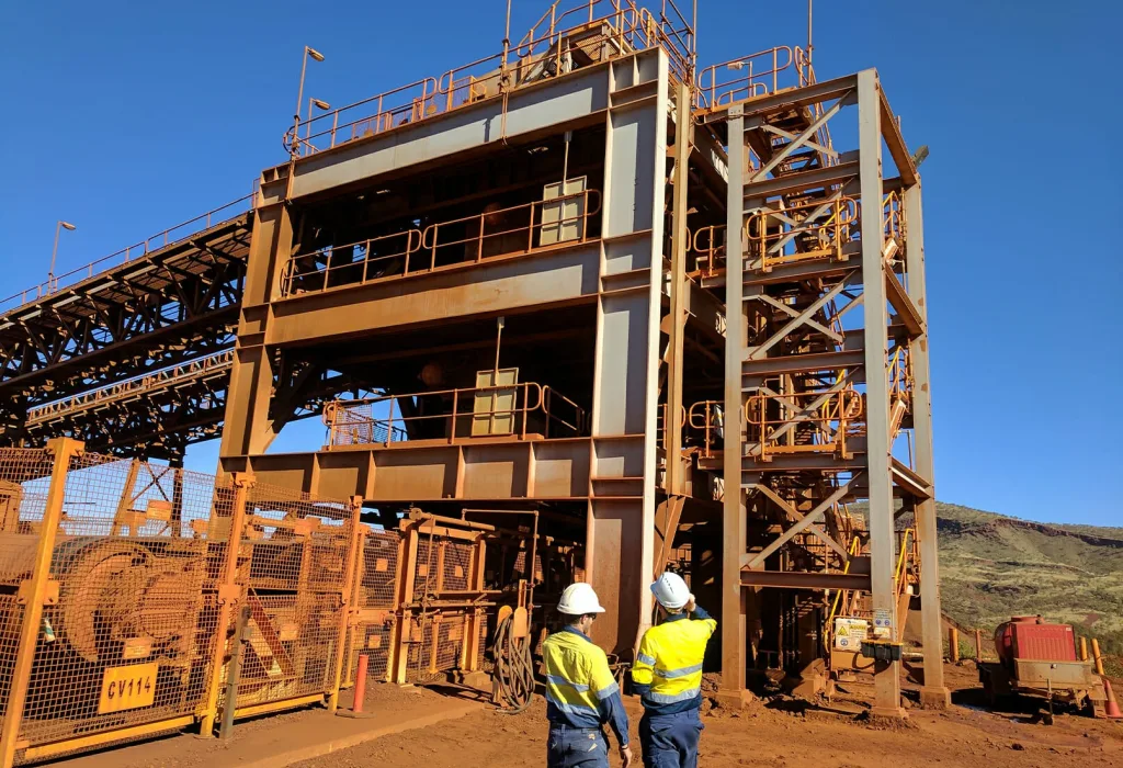 Two EMtek team members stand in front of a large structure, observing the Weba chute replacement project for Fortescue in the Pilbara.