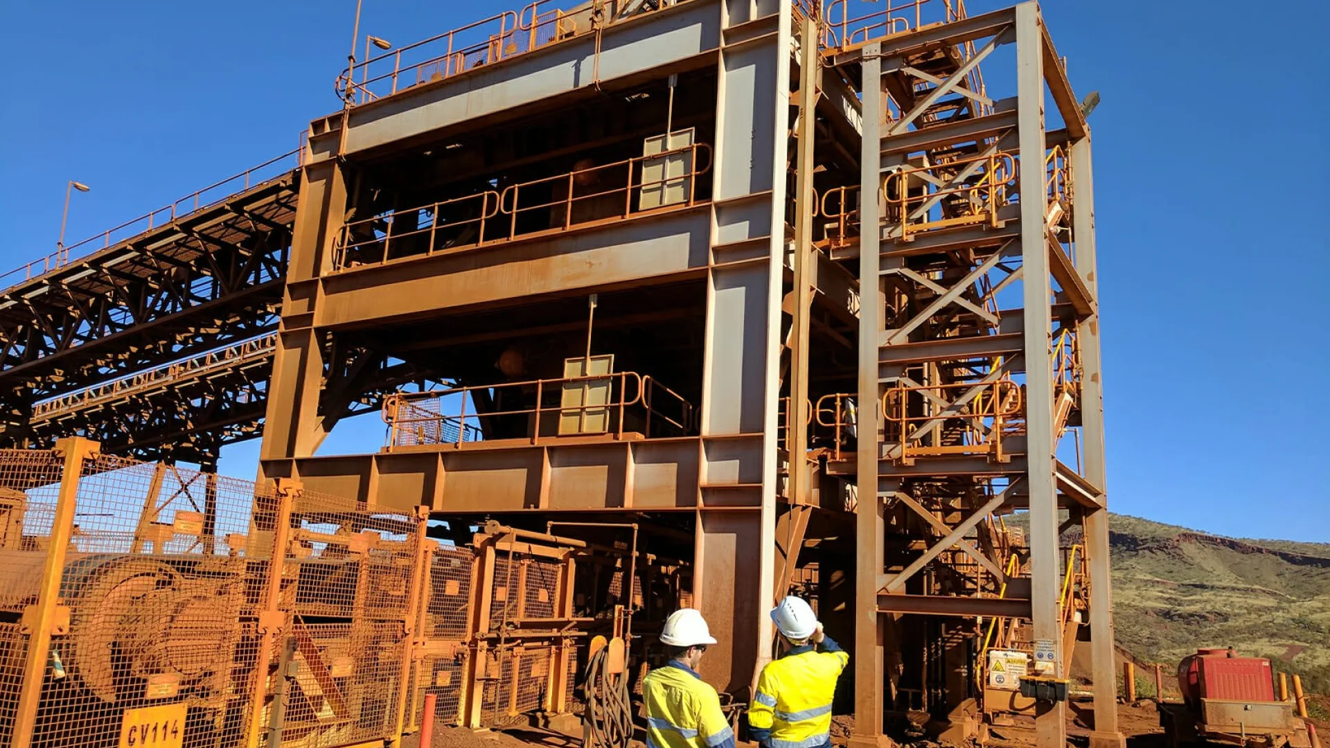 Two EMtek team members stand in front of a large structure, observing the Weba chute replacement project for Fortescue in the Pilbara.