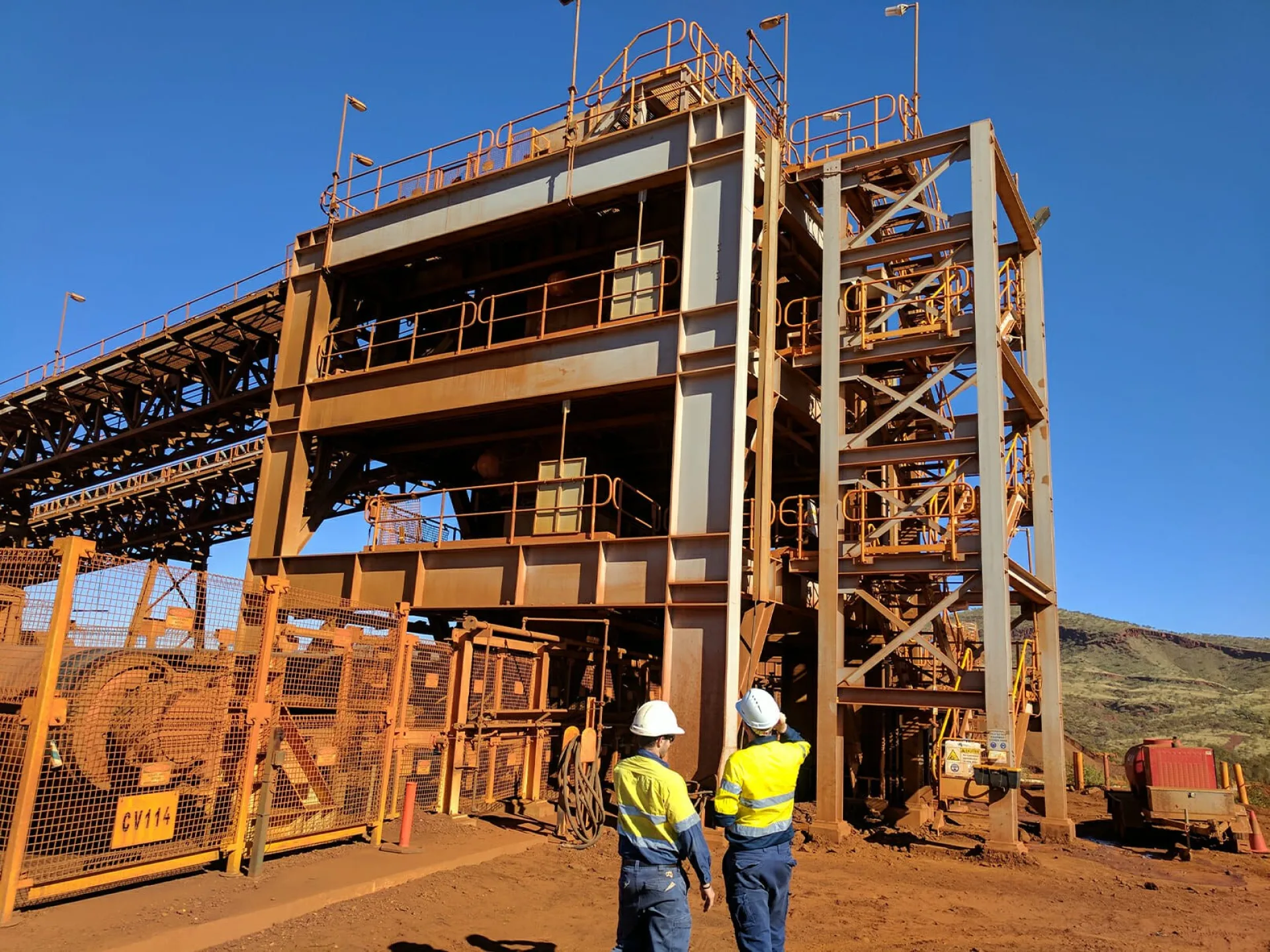 Two EMtek team members stand in front of a large structure, observing the Weba chute replacement project for Fortescue in the Pilbara.