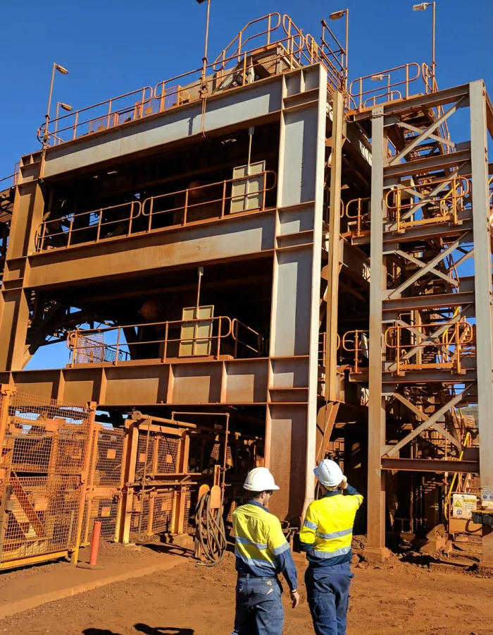 Two EMtek team members stand in front of a large structure, observing the Weba chute replacement project for Fortescue in the Pilbara.